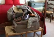 Valise ouverte sur une table, vêtements roulés et check‑list près d'une fenêtre en plein jour