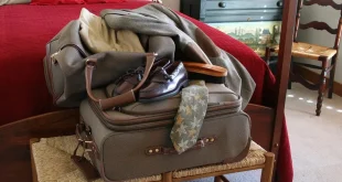 Valise ouverte sur une table, vêtements roulés et check‑list près d'une fenêtre en plein jour