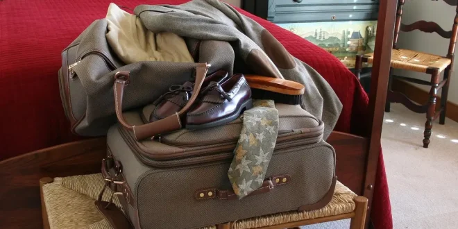 Valise ouverte sur une table, vêtements roulés et check‑list près d'une fenêtre en plein jour