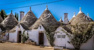 Rue pavée aux maisons blanches et trulli en arrière-plan, petit café en terrasse