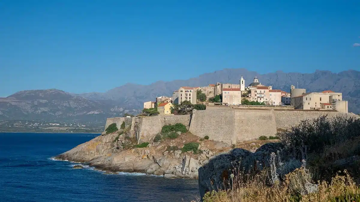 Littoral corse montrant contraste entre côte ensoleillée et montagnes en arrière-plan