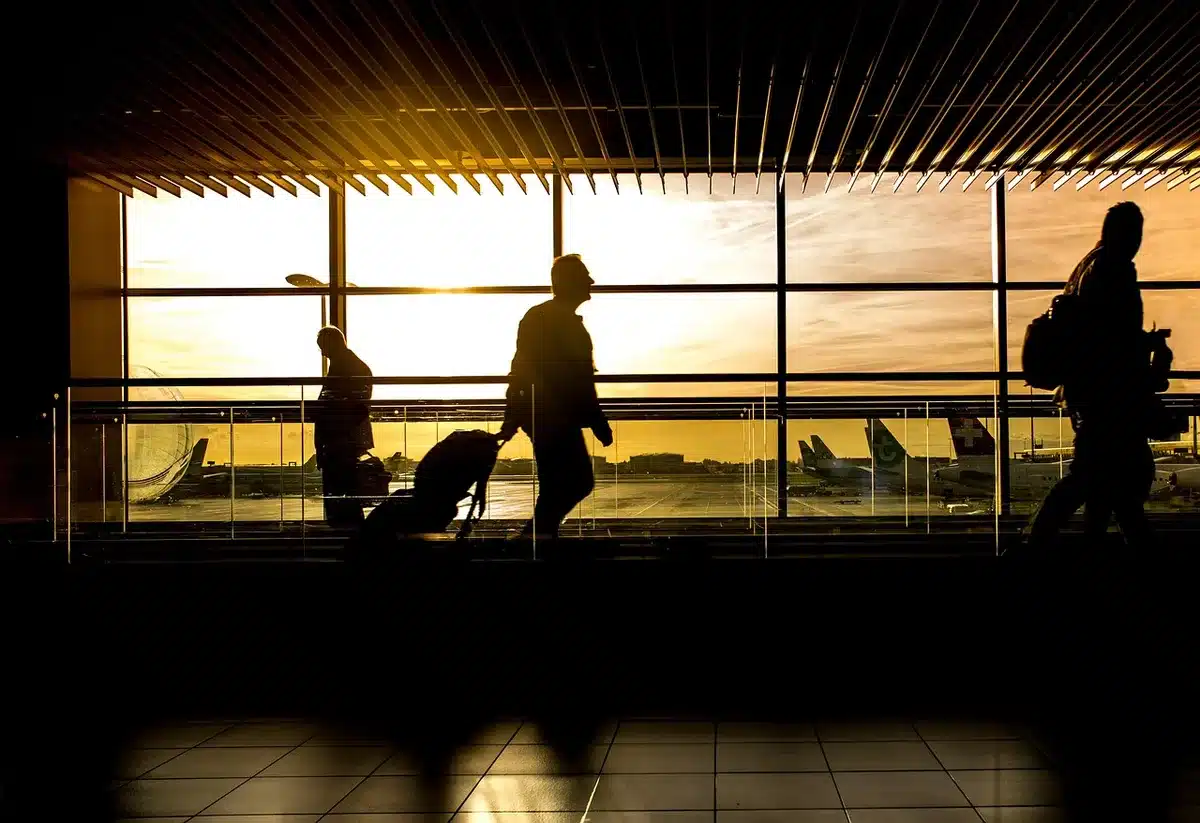 Personne vérifiant le statut d'un vol sur un téléphone avec l'écran d'aéroport en arrière-plan